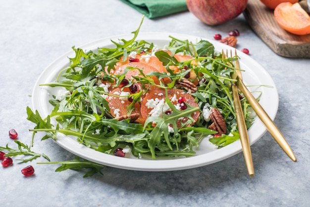 Persimmon salad with arugula, nuts, goat cheese, pomegranate. Healthy vegetarian food salad concept.