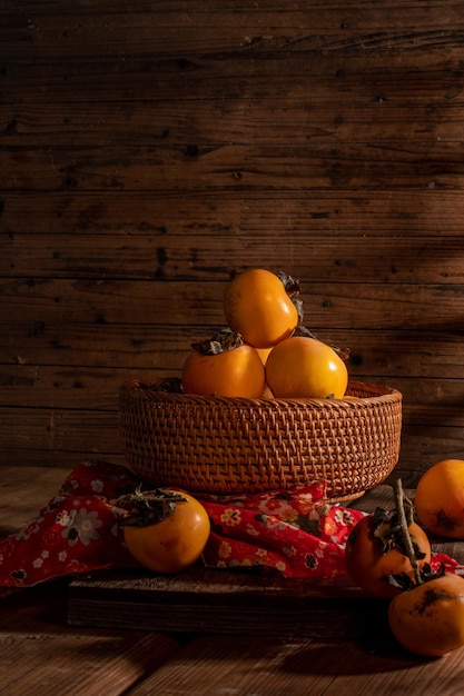 Persimmons on the plate are on the wooden table in dark light