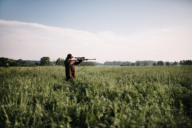 Foto persona che mira con una pistola in mezzo all'erba sul campo