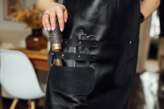 Person in black apron with professional hairdresser set on dark background closeup