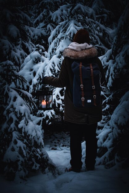 Foto persona che porta lanterna e zaino nella foresta invernale