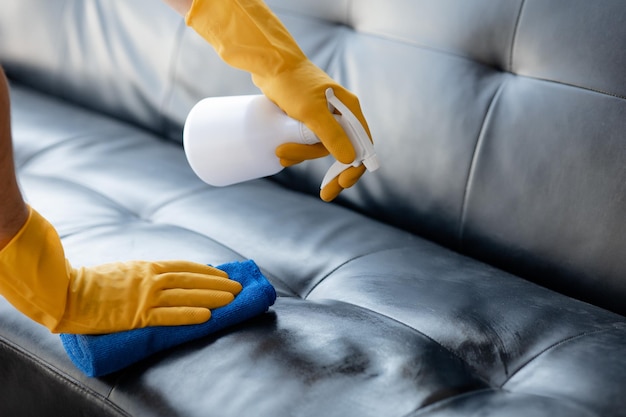 Человек, убирающий комнату, уборщик использует ткань и распыляет дезинфицирующее средство, чтобы протереть диваны в офисе компании Уборщик Поддержание чистоты в организации