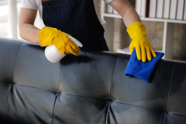 Person cleaning the room cleaning staff is using cloth and spraying disinfectant to wipe the sofas in the company office room Cleaning staff Maintaining cleanliness in the organization