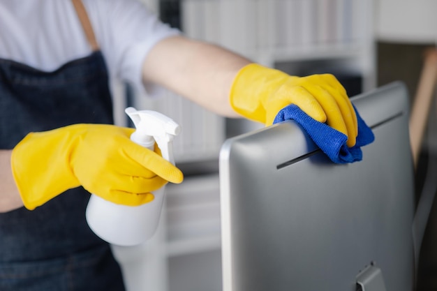 Person cleaning room cleaning worker is using cloth to wipe computer screen in company office room Cleaning staff Concept of cleanliness in the organization