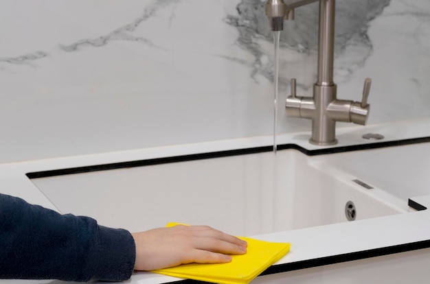 A person cleaning a sink with a yellow rag.