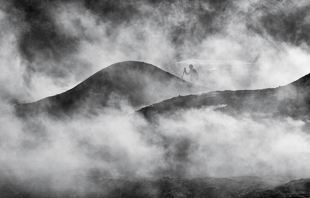 person climbing on mountain against sky during foggy weather