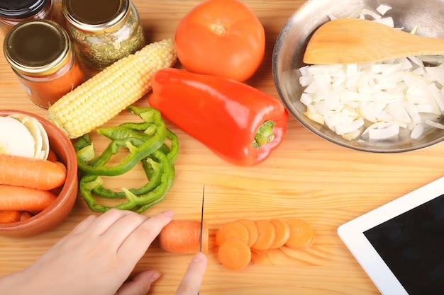 Person cutting a carrot with vegetables and digital tablet.