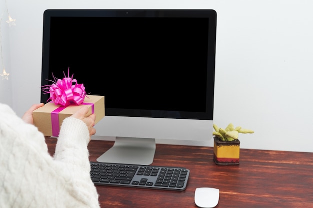 Person delivering a gift in front of the computer. Computer with black screen for text or photo. Mockup.