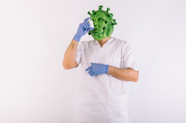 Person disguised as a coronavirus with a latex mask  covid19 virus, wearing a doctors suit, taking an asthma inhaler, on white background.