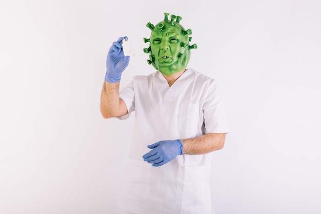 Persona travestita da coronavirus con una maschera in lattice virus covid19, che indossa una tuta da medico, assume un inalatore per l'asma, su sfondo bianco.