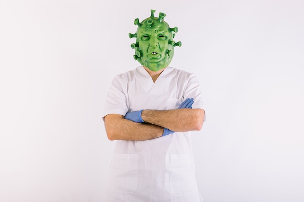 Person disguised as coronavirus with latex mask  covid19 virus, wearing doctors suit with arms crossed arms on white background