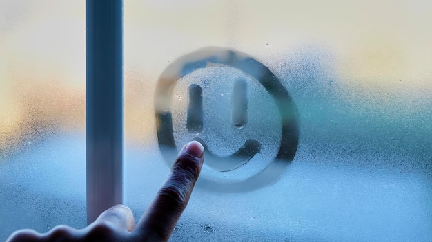 Photo person drawing a smiley face on the window on a winter day