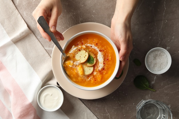 Person eating pumpkin soup on grey table, top view