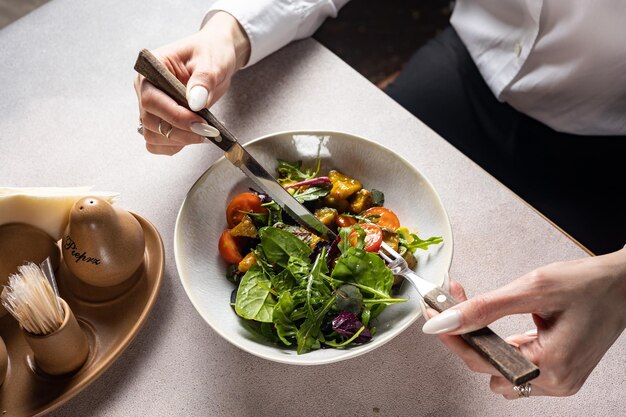 A person eating a salad with a fork and knife.