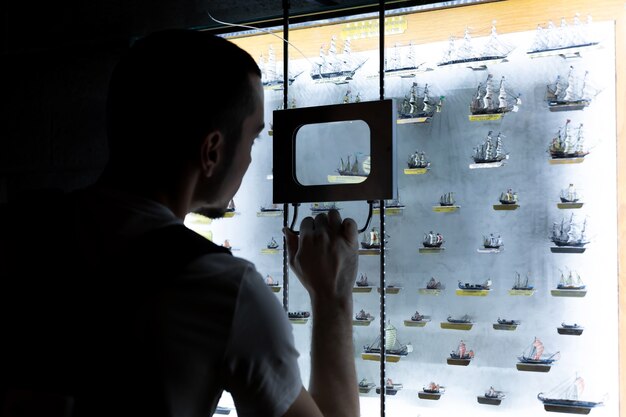 Person examines models of ships through a magnifying glass. An exhibit in the museum.