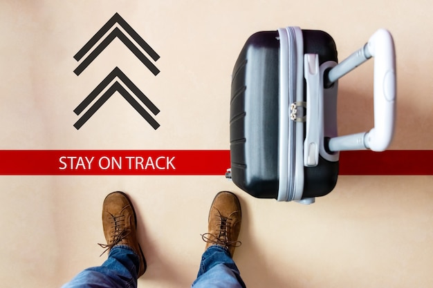 Person following the direction of the mark on the floor with a black suitcase