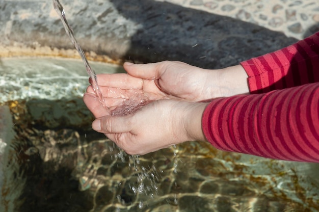 A person at a fountain collects water in his hands to drink