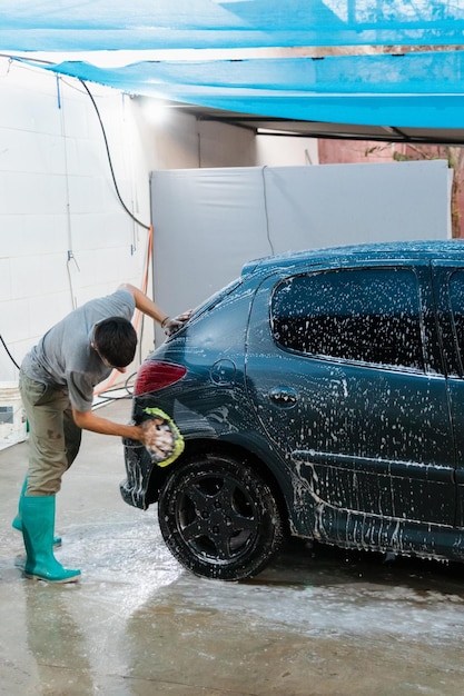 A person from behind washing the back of a car full of foam