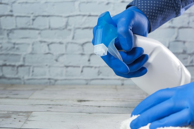 Person hand in disposable gloves using disinfectant spray to clean table surface