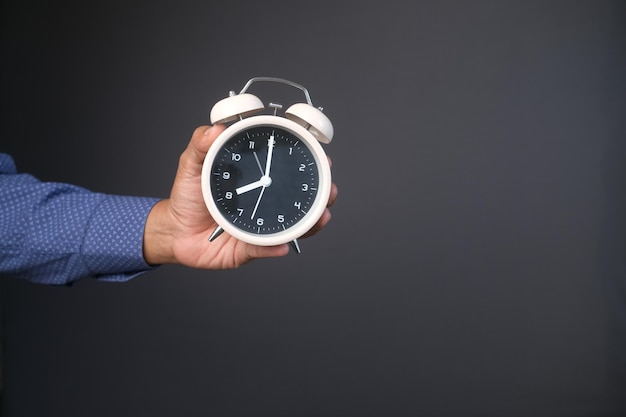 person hand holding alarm clock against gray background