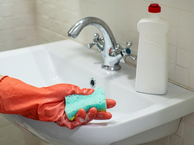 Person hand holding a mint sponge for cleaning bathroom sink and faucet