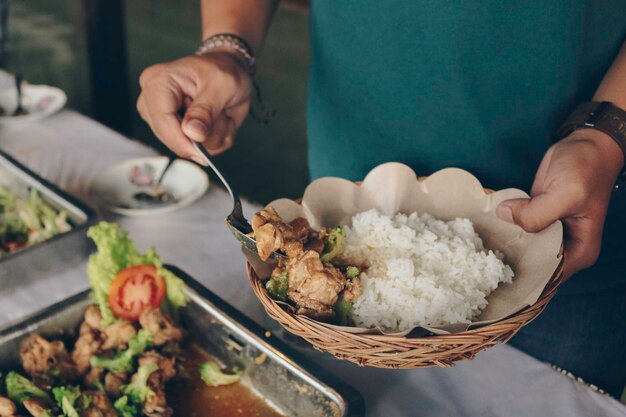 レストランでの昼食時に、人の手がチキン焼肉をスティールパンから木製の紙皿に置きます