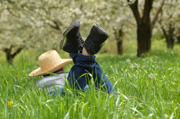 A person in hat lying down on green field with flowers