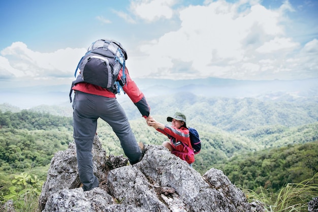 Person hike friends helping each other up a mountain Man and woman giving a helping hand and active fit lifestyle Asia couple hiking help each other concept of friendship teamwork