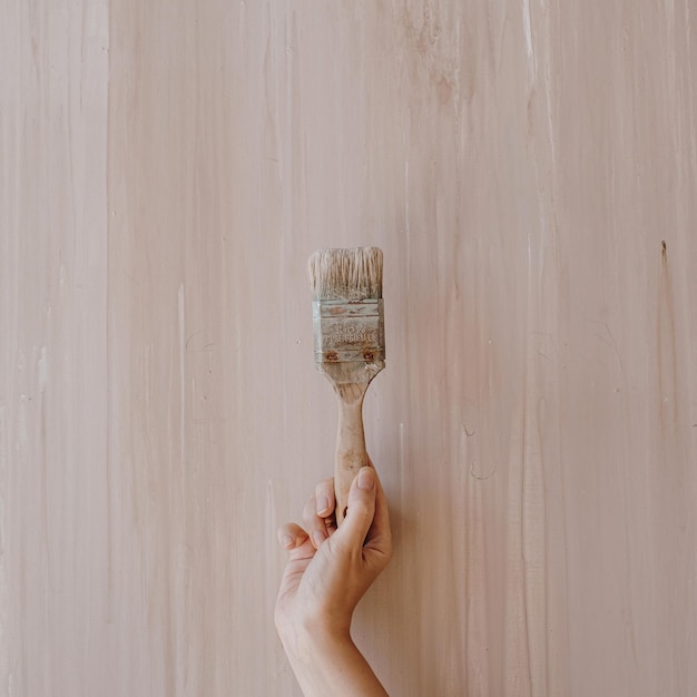 Person hold paint brush on neutral pastel pink background