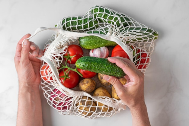 A person holding a bag of vegetables with a cucumber in it.