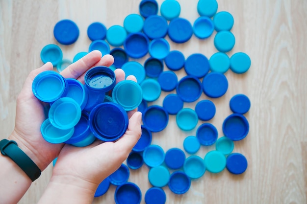 Persona che tiene i tappi delle bottiglie sullo sfondo dei tappi delle bottiglie di plastica blu concetto di riciclaggio