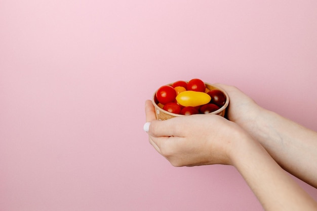 Person holding a bowl of tomatoes on a pink background