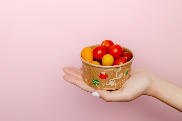 Person holding a bowl of tomatoes on a pink background