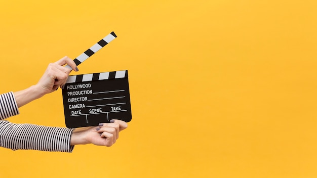 Photo person holding a clapper board on yellow background