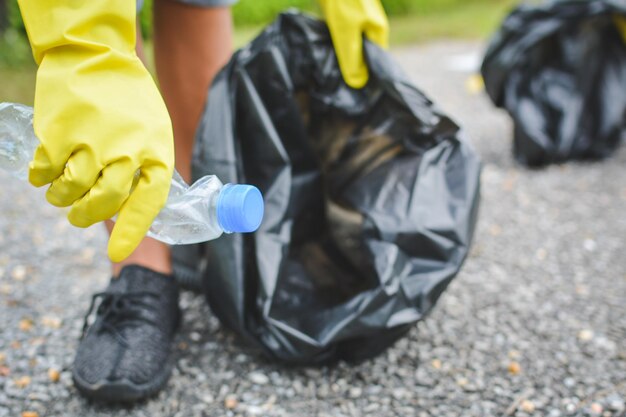 Photo person holding crushed plastic bottle and garbage bag while standing on street