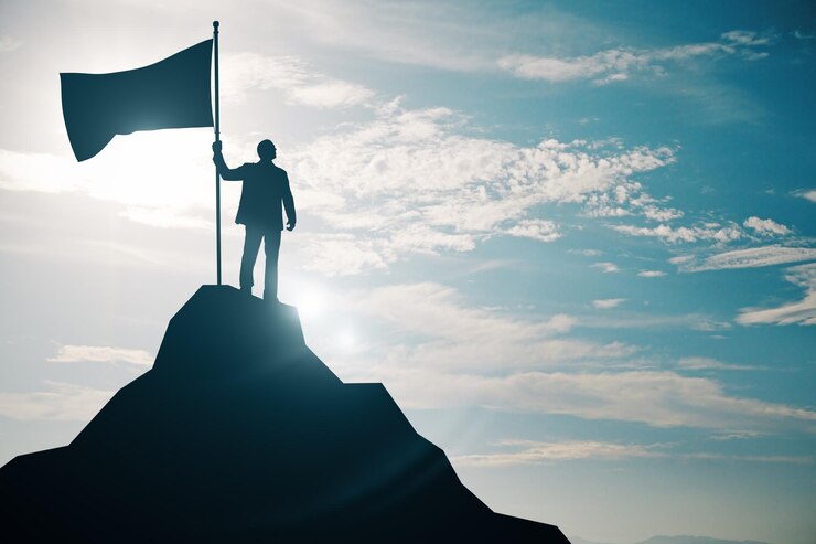 Photo person holding a flag on top of a mountain peak silhouetted against the sky symbolizing victory and achievement