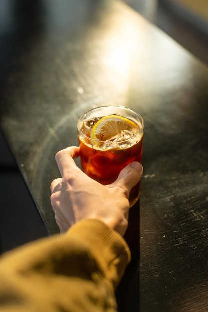 A person holding a glass of iced tea with lemon on the top.