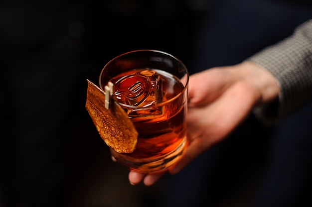 Person holding a glass of whiskey with ice