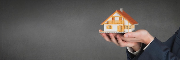 Persona in possesso di una casa su sfondo grigio come concetto di assicurazione casa