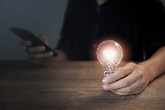 A person holding a light bulb with a phone in the background