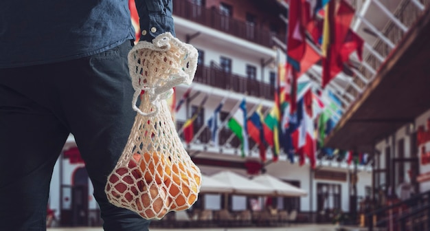 A person holding a mesh eco bag with fresh fruit food from grocery store