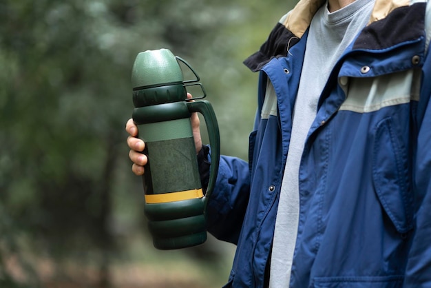 A person holding a metal thermos with hot water outdoors