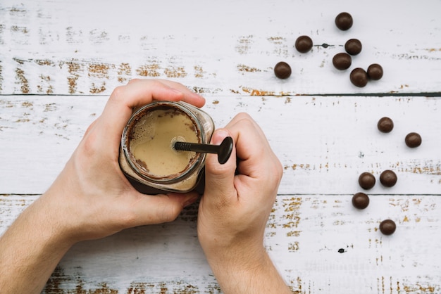 A person holding milkshake in jar with chocolate balls on wooden table