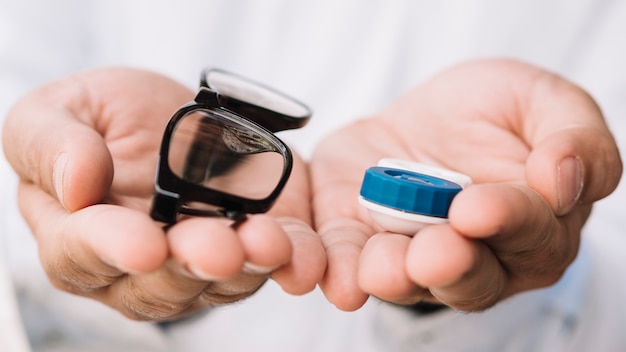 Person holding a pair of black glasses and contact lens