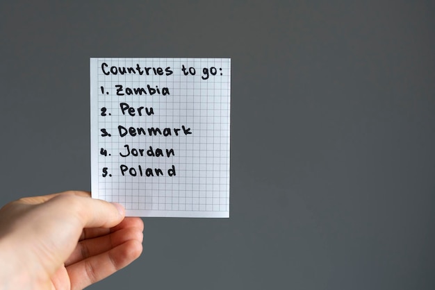 A person holding a paper note with countries to visit list