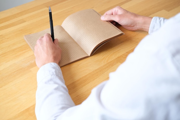 Person holding a pen in his hand and opens notebook with kraft sheets close up