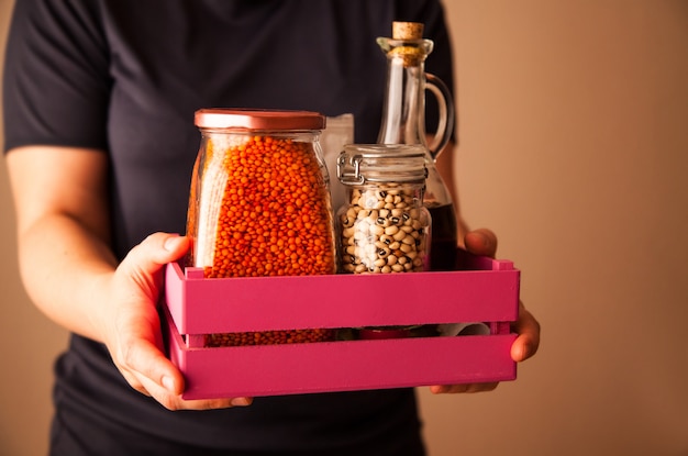 Person holding a pink wooden box with groats beans and lentils and olive oil.