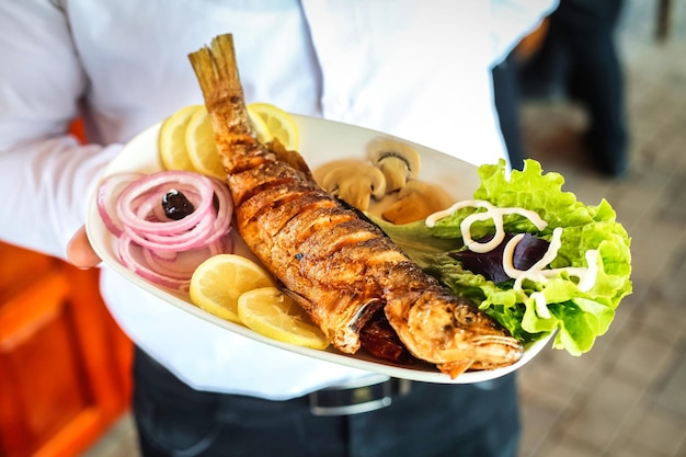 夕食に魚の皿を握っている人