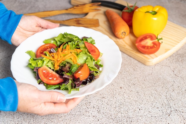 A person holding a plate of salad with tomatoes and cheese