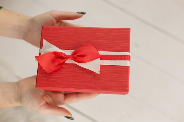 A person holding a red gift box with a red bow.